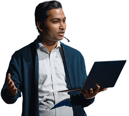 Male conference speaker wearing a headset microphone and holding a laptop computer.